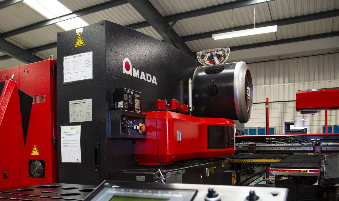 Close-up of an industrial AMADA CNC punching machine in a factory setting, showing its red and black exterior and control panel.