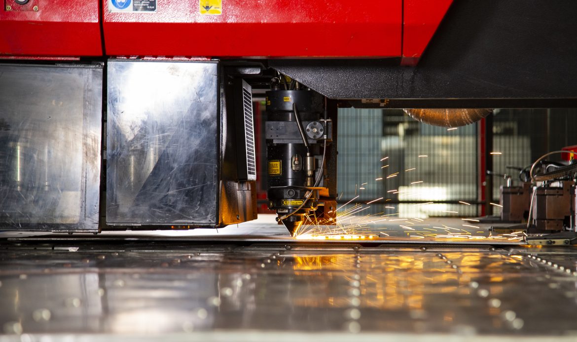 Close-up view of an industrial laser cutting machine in operation, emitting bright sparks as it cuts through a sheet of metal in a factory setting.