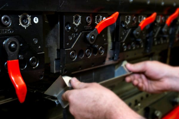 Close-up of hands adjusting a metal part under red-handled levers on a machine press.
