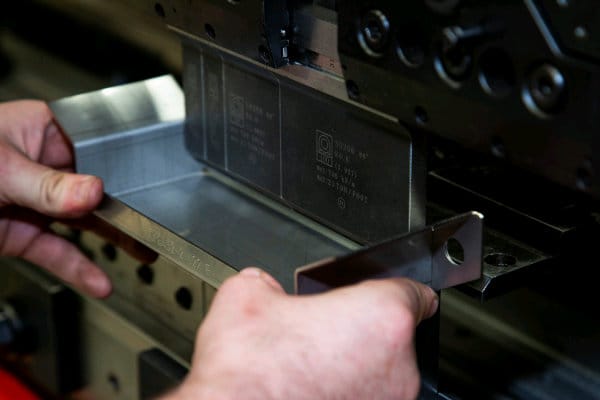 Close-up of hands adjusting a metal component on an industrial press brake machine.