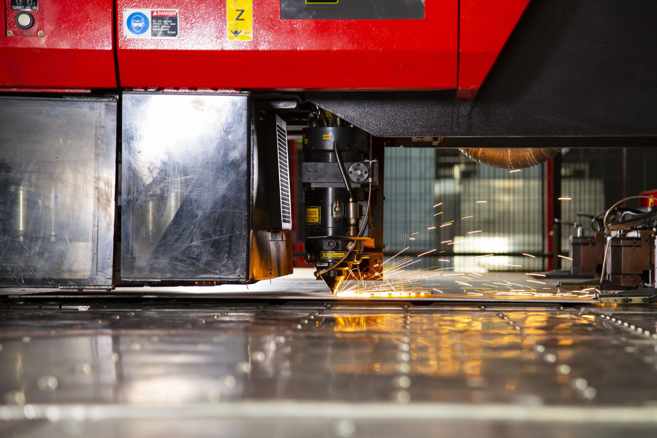 Close-up view of an industrial laser cutting machine in operation, emitting bright sparks as it cuts through a sheet of metal in a factory setting.